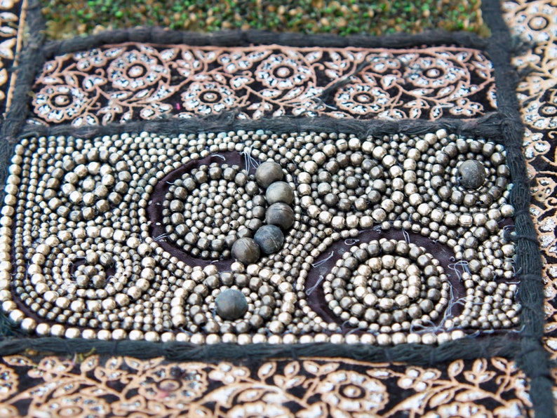 May include: A close-up of a black fabric with silver beads sewn in a circular pattern. The beads are arranged in a swirling design, creating a decorative and intricate look.