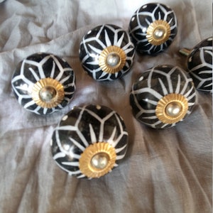 Peut inclure: Six boutons de porte en céramique noire et blanche avec un motif géométrique et des accents dorés.