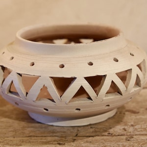 May include: White ceramic candle holder with a geometric design. The holder has a round base and a wide opening at the top.
