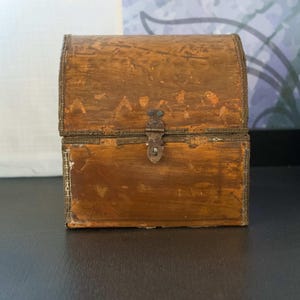 May include: A small, antique wooden chest with a curved top and metal accents. The chest is a warm brown color with visible wood grain and a metal clasp. The chest is likely used for storage and decorative purposes.