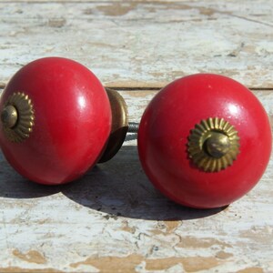 Può includere: Due pomelli per armadi in ceramica rossa con dettagli dorati. I pomelli hanno un design circolare rialzato al centro.