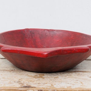 Puede incluir: Un tazón de madera grande y rojo con un fondo ligeramente redondeado y un borde ancho y plano. El tazón tiene un aspecto rústico y artesanal.