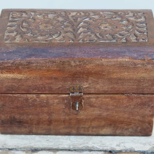 Puede incluir: Una pequeña caja de madera con un diseño floral tallado en la tapa. La caja tiene un cierre de latón y está hecha de madera marrón oscura.