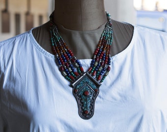 May include: A multi-strand necklace with a large silver pendant. The necklace is made of red, blue, green, and white beads. The pendant is decorated with turquoise and coral.