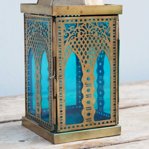 May include: A brass lantern with a blue glass panel and intricate cut-out designs. The lantern has a square base and a hinged door.