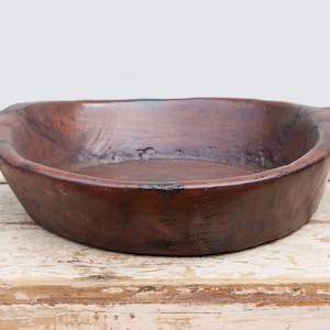 Puede incluir: Un cuenco de madera grande, de forma ovalada, con dos asas. El cuenco es de color marrón oscuro y tiene un aspecto rústico y envejecido.