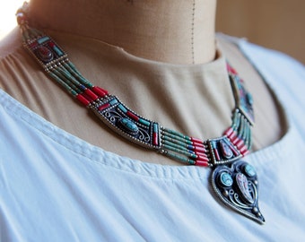 May include: A multi-strand necklace with a large, ornate pendant. The necklace is made of silver and features turquoise, coral, and other stones. The pendant is shaped like a heart and has a detailed design.