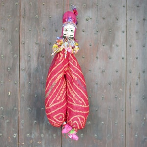 Puede incluir: Un títere tradicional indio con un atuendo estampado en rojo y dorado. El títere tiene una cara pintada con bigote y turbante.