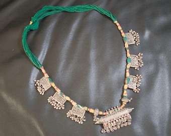 May include: A silver necklace with a green and cream cord and multiple silver pendants. The pendants are rectangular with intricate designs and have small silver beads hanging from them.