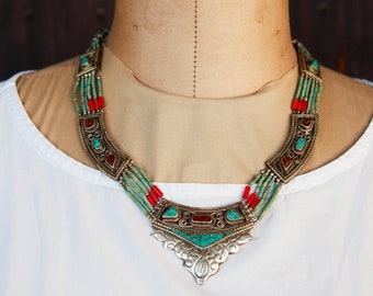 May include: A silver necklace with turquoise and red coral beads. The necklace has a large, ornate pendant with a floral design.