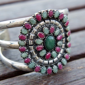 Könnte beinhalten: Ein silbernes Armband mit einem runden Design, das mit rosa und grünen Steinen besetzt ist. Das Armband hat drei Bänder.