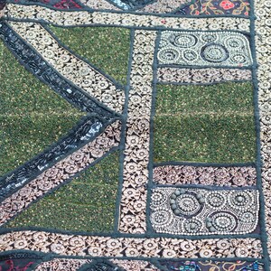 May include: A green and black patchwork tapestry with intricate embroidery and beaded details. The tapestry features a variety of geometric shapes and patterns, including circles, squares, and triangles.