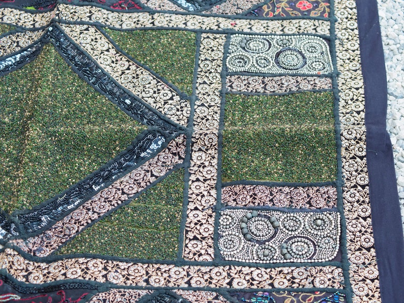 May include: A green and black patchwork tapestry with intricate embroidery and beaded details. The tapestry features a variety of geometric shapes and patterns, including circles, squares, and triangles.