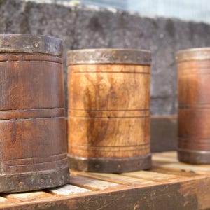 Könnte beinhalten: Drei Holzbehälter mit Metallbändern um Ober- und Unterseite. Die Behälter sind unterschiedlich groß und haben eine natürliche Holzoptik.