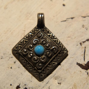 Może przedstawiać: Srebrny wisiorek z turkusowym kamieniem w środku. Wisiorek ma kształt diamentu i ozdobiony jest misternymi wzorami wokół kamienia.