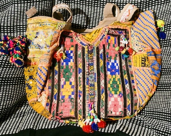 Puede incluir: Una bolsa de mano de patchwork colorida con una variedad de telas y bordados. La bolsa tiene un asa de cuero marrón y está decorada con borlas y cuentas.