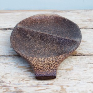 Puede incluir: Una fuente de madera ovalada, de color marrón oscuro, con superficie texturizada. Dividida en dos secciones y con un asa. La veta de la madera es visible, lo que le da un encanto rústico. Ideal para servir aperitivos o porciones pequeñas. Mide aproximadamente 25 cm de largo.