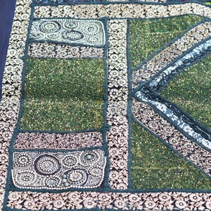 May include: A patchwork tapestry with a green background and intricate floral patterns in black, white, and gold. The tapestry is made of different fabrics and textures, and it has a unique and handmade look.