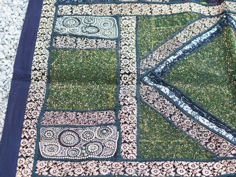 May include: A patchwork tapestry with a green background and intricate floral patterns in black, white, and gold. The tapestry is made of different fabrics and textures, and it has a unique and handmade look.