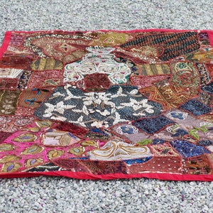 Puede incluir: Una colcha de retazos colorida con bordados y abalorios intrincados. La colcha está hecha de varias telas en tonos de rojo, marrón, rosa, azul y verde. La colcha está decorada con lentejuelas, cuentas y otros adornos.