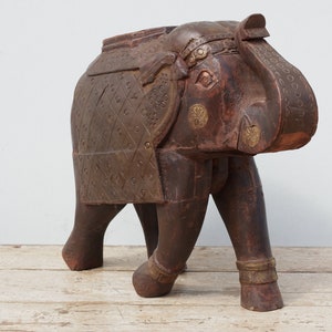 Può includere: Una scultura di elefante in legno marrone scuro con dettagli dorati. L'elefante è in piedi su tutte e quattro le zampe e ha la proboscide sollevata in aria. La scultura è finemente scolpita con dettagli sul corpo e sul viso dell'elefante.
