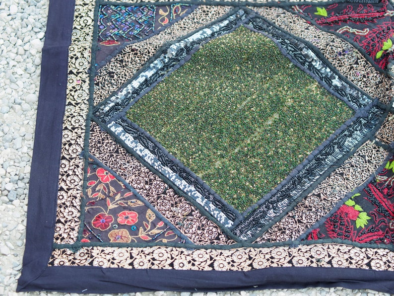 May include: A square throw pillow with a black background and a diamond-shaped green center. The diamond is surrounded by a black and silver trim. The pillow is made of fabric and has a variety of colorful embroidered details.