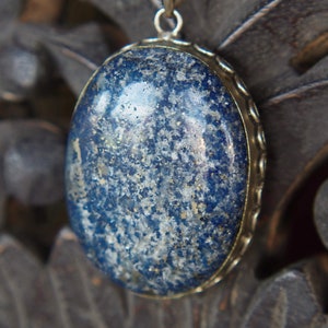 Może przedstawiać: Srebrny wisiorek z dużym owalnym kamieniem lapis lazuli. Kamień jest ciemnoniebieski z białymi plamkami.