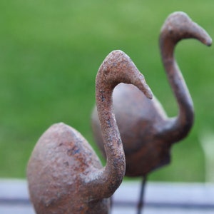 May include: Two rusty metal bird sculptures with long necks and curved beaks. The sculptures are standing on a wooden surface.
