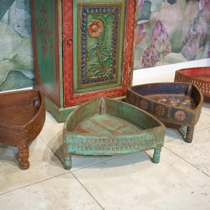 Peut inclure: Quatre plateaux décoratifs triangulaires en bois avec de petits pieds. Les plateaux sont peints en marron, vert, bleu et rouge. Un grand meuble orné avec un motif floral se trouve en arrière-plan. Idéal pour la décoration.