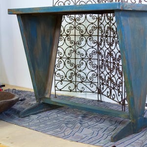 Op de afbeelding: Een blauw geschilderde houten console met een rechthoekig blad en schuine poten. De tafel heeft een verweerde afwerking, met zichtbare penseelstreken. De tafel is ongeveer 122 cm lang en 41 cm breed.