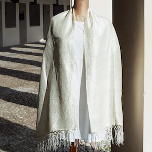 Peut inclure: Une écharpe en soie crème avec une surface texturée et une bordure à franges. L'écharpe est drapée sur un mannequin blanc, mettant en valeur son drapé élégant et son éclat subtil. La frange délicate ajoute une touche de sophistication.