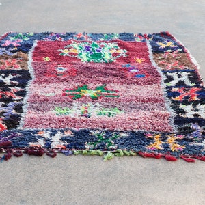 Puede incluir: Una alfombra marroquí colorida con una variedad de patrones y colores, incluyendo rojo, azul, verde y negro. La alfombra tiene un borde con flecos y está hecha de lana.