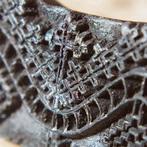 Könnte beinhalten: Nahaufnahme einer dunkelgrauen, strukturierten und kompliziert gemusterten Oberfläche. Die Oberfläche hat ein erhabenes, geometrisches Design mit einem sich wiederholenden Muster aus Quadraten und Linien.