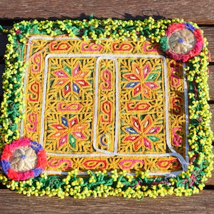 Peut inclure: Un coussin carré brodé avec un motif floral coloré et une bordure perlée. Le coussin est fait d'un tissu jaune avec un fond vert et a une bordure blanche. Les perles sont vertes et jaunes.