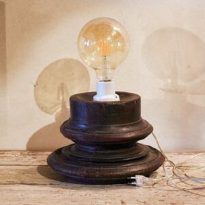 May include: A rustic wooden lamp base with a clear glass light bulb and a white cord. The lamp is on a light wood surface.