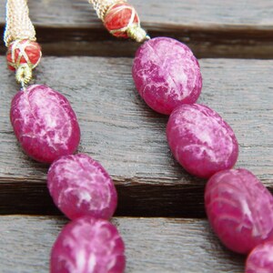 May include: A pink and white oval-shaped beaded necklace with a gold chain and red accents.