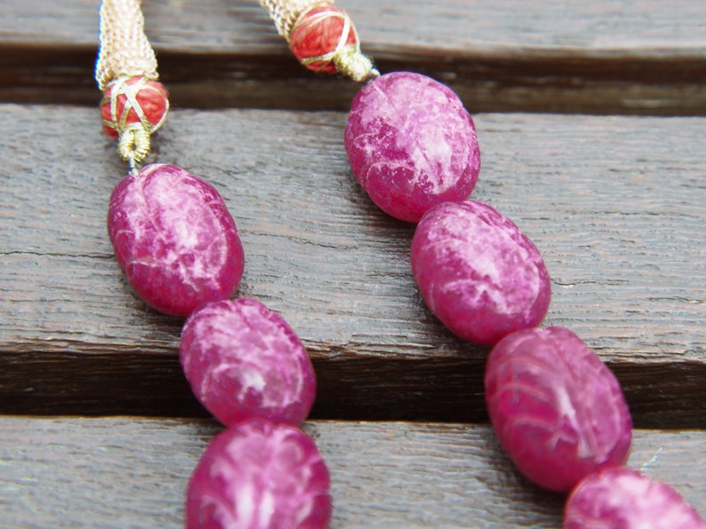 May include: A pink and white oval-shaped beaded necklace with a gold chain and red accents.