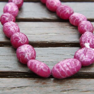 May include: A strand of pink oval-shaped beads with white marbling. The beads are strung on a white cord.