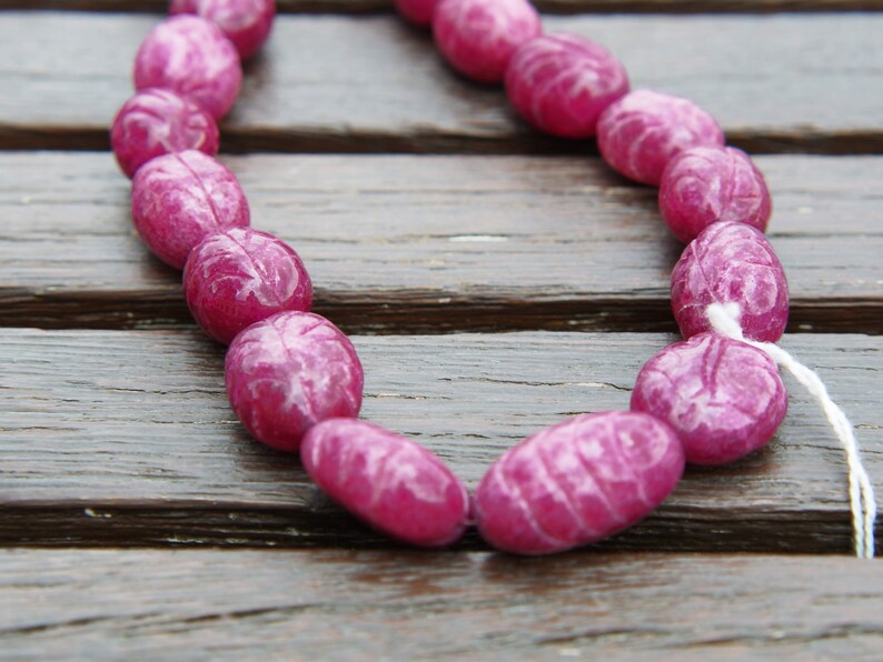 May include: A strand of pink oval-shaped beads with white marbling. The beads are strung on a white cord.