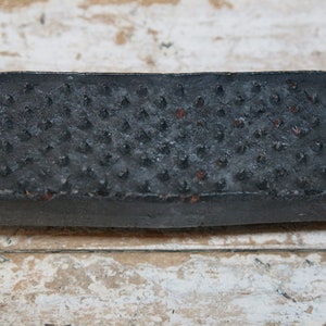 Puede incluir: Una barra de jabón rectangular negra con una superficie texturizada. El jabón tiene una textura rugosa y abultada.