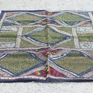 May include: A patchwork quilt with a diamond pattern in shades of green, black, and red. The quilt is decorated with sequins and embroidery.