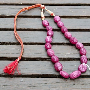 May include: A pink gemstone necklace with a red tassel. The necklace is made of oval-shaped beads and is strung on a thin cord.