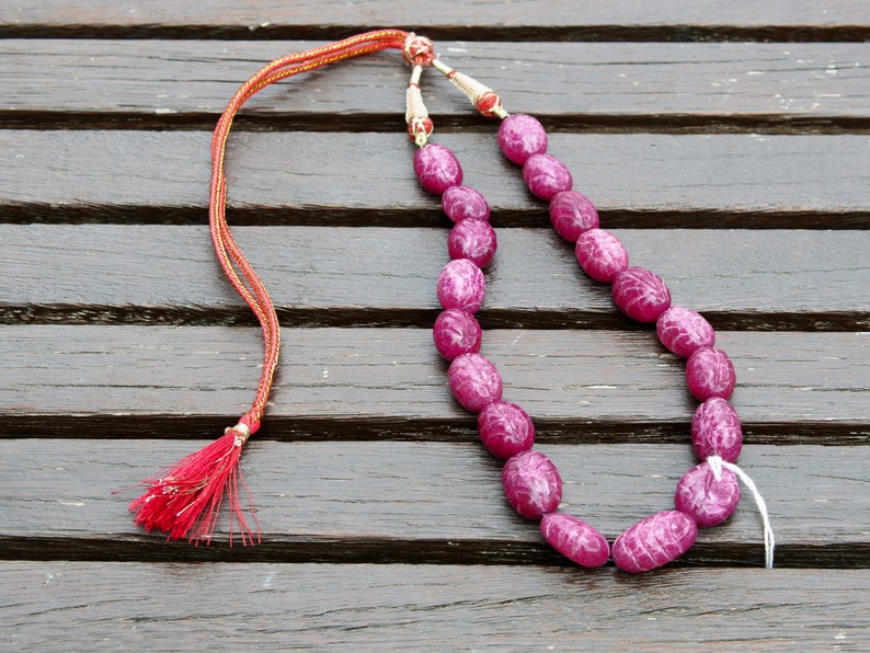 May include: A pink gemstone necklace with a red tassel. The necklace is made of oval-shaped beads and is strung on a thin cord.