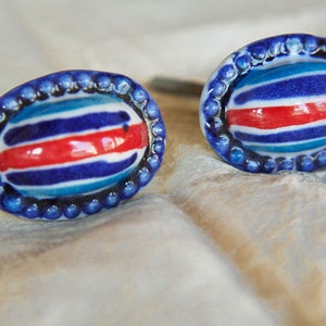 Op de afbeelding: Twee blauwe en witte gestreepte keramische knoppen met een rode streep en een parelrand.