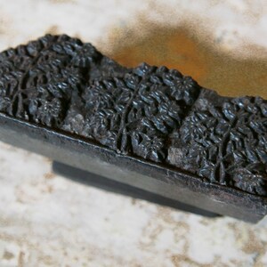 May include: A vintage wooden printing block with a carved floral design. The block is dark brown and has a rectangular shape.