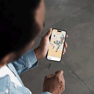 Puede incluir: Una persona sostiene un tel&eacute;fono inteligente que muestra un mapa de la ciudad con varios marcadores de ubicaci&oacute;n de colores. El tel&eacute;fono tiene un marco negro y una pantalla blanca. La persona lleva una camisa vaquera.
