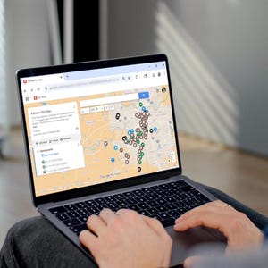 Puede incluir: Una computadora portátil muestra un mapa de Kansas City con numerosos marcadores de ubicación. La pantalla muestra una interfaz de Google Maps con una lista de restaurantes y otros puntos de interés. Las manos del usuario son visibles en el teclado.