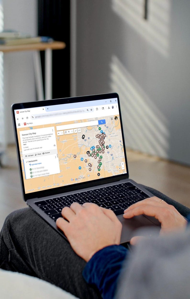Puede incluir: Una computadora port&aacute;til muestra un mapa de Kansas City con numerosos marcadores de ubicaci&oacute;n. La pantalla muestra una interfaz de Google Maps con una lista de restaurantes y otros puntos de inter&eacute;s. Las manos del usuario son visibles en el teclado.