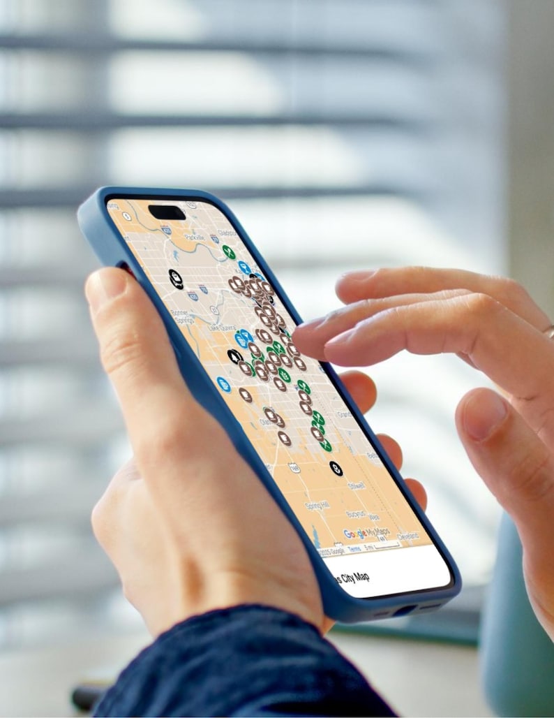 Puede incluir: Un smartphone con una funda azul muestra un mapa con numerosos marcadores de ubicaci&oacute;n. La pantalla muestra un mapa detallado de la ciudad con varios iconos de colores, que sugieren puntos de inter&eacute;s o ubicaciones. Una mano toca la pantalla.
