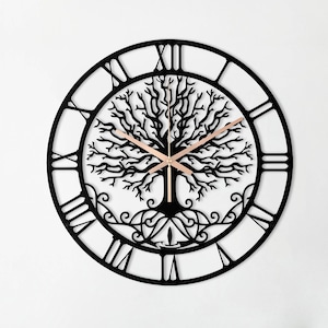 May include: Black metal wall clock with Roman numeral markings and a tree of life design. The clock is hanging on a white wall above a wicker sofa with colorful throw pillows.